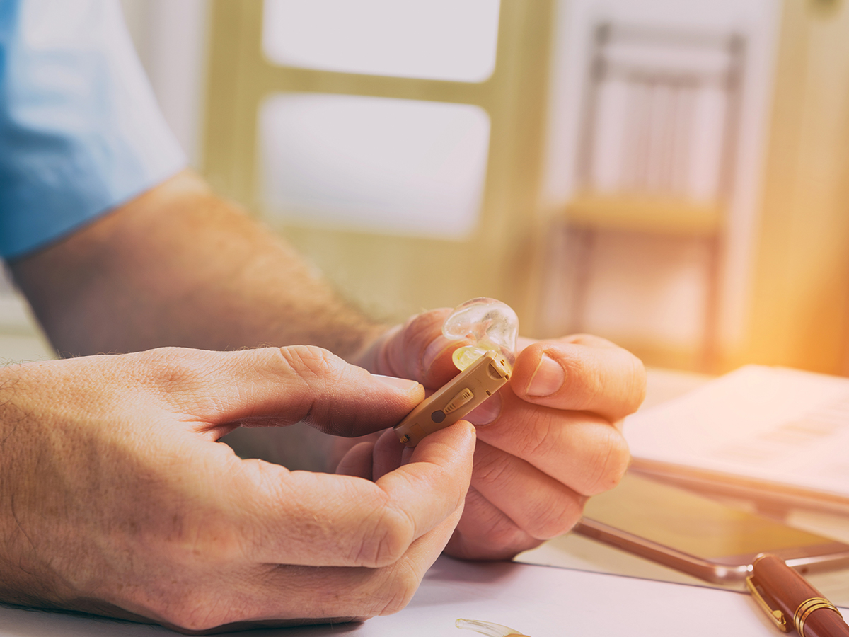 Man holding hearing aid at a desk.