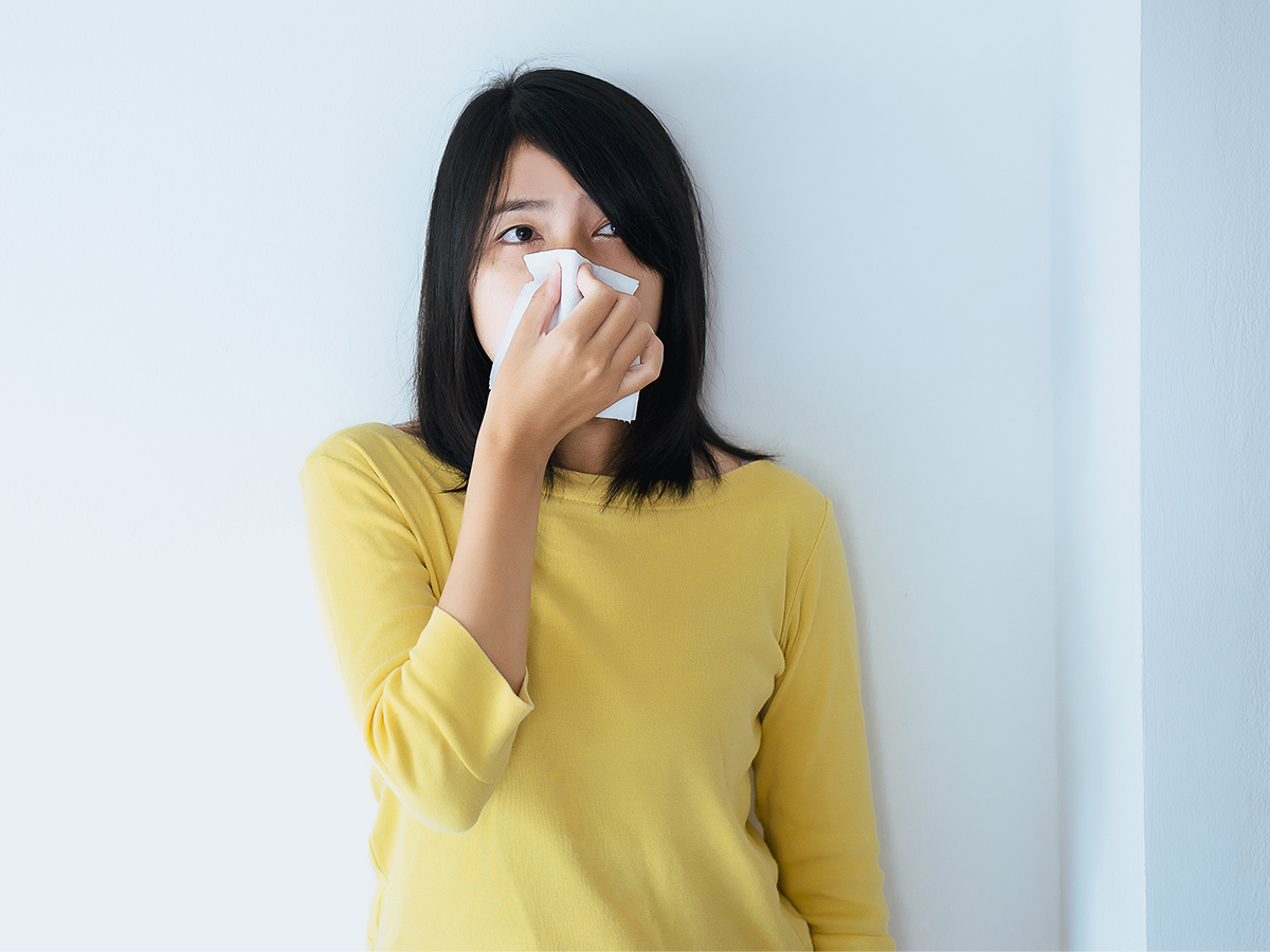Woman in yellow sweater holding tissue to her nose