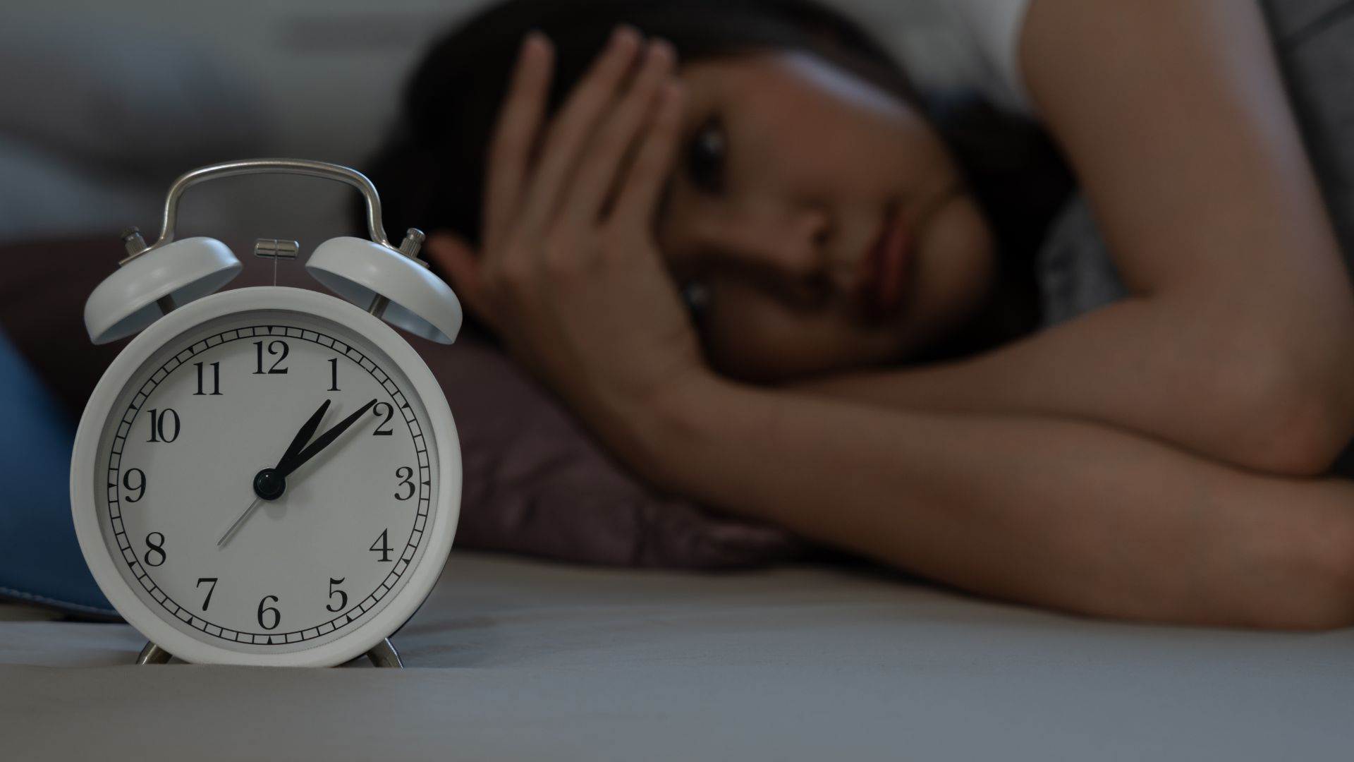 a woman laying in bed next to a clock