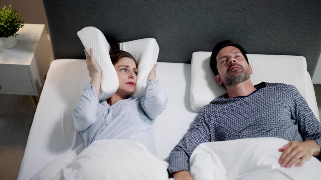 a wife covering her ears as her husband snores